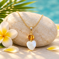 Collar de ámbar con corazón de madreperla sobre piedra clara con flor de frangipani, hoja de palma y pétalos
