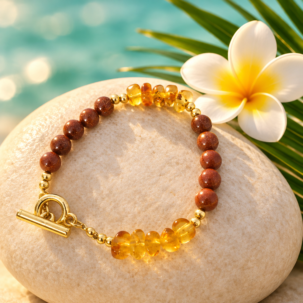 Pulsera de arena dorada y ámbar con baño de oro sobre piedra clara con flor de frangipani y hoja de palma