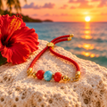 Pulsera de cordón de coral rojo y larimar sobre piedra coralina al atardecer, con flor de hibisco