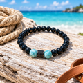 Pulsera de larimar y ónix con detalle de cristal sobre madera clara en la playa, con cuerda y cuero