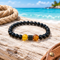 Pulsera de ámbar y ónix con detalle de cristal sobre madera clara en la playa, con cuerda y cuero