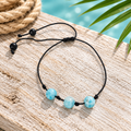Pulsera de hilo con bola de larimar sobre madera clara con cuerda y hoja de palma