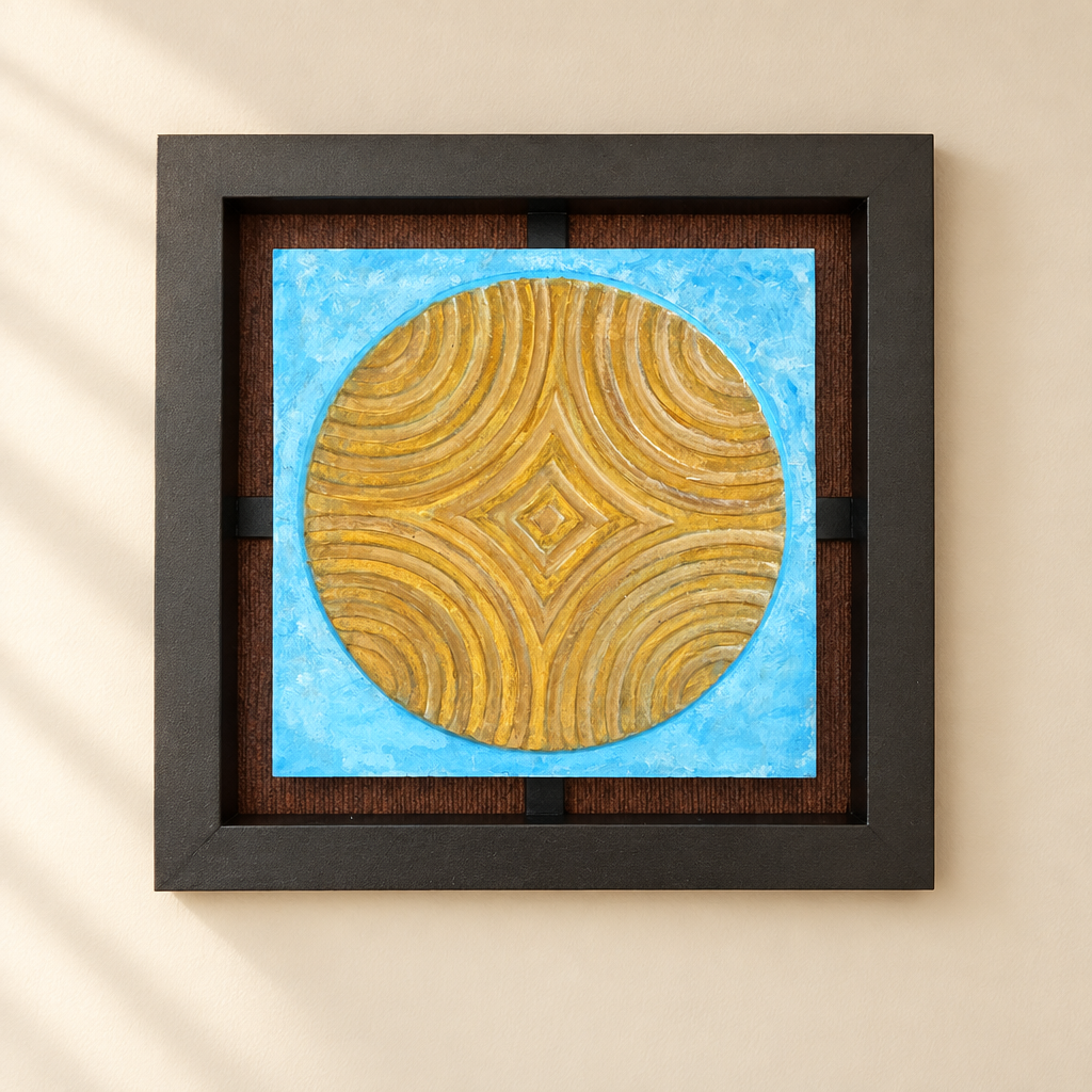 Cuadro decorativo de metal con motivo circular dorado sobre fondo azul, enmarcado en un ambiente luminoso de pared crema.