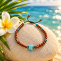 Pulsera de arena dorada, larimar y turquesa sobre piedra clara con flor de frangipani y hoja de palma, mar Caribe de fondo