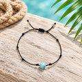Pulsera unisex de hilo y larimar sobre madera clara con cuerda y hoja de palma